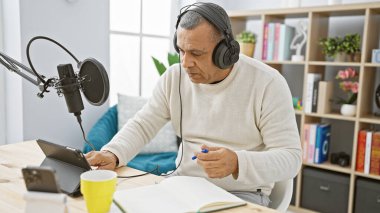 Olgun bir İspanyol, mikrofon ve kulaklıklarla donatılmış bir stüdyoda podcast kaydediyor..