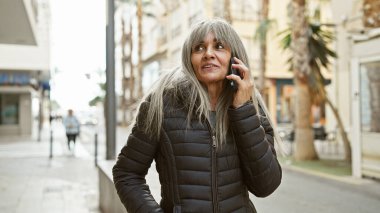Şehir caddesinde telefonla konuşan, gri uzun saçlı, olgun İspanyol kadın..