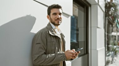 Şehir sokaklarında sakallı yakışıklı İspanyol bir adam akıllı telefon tutuyor..