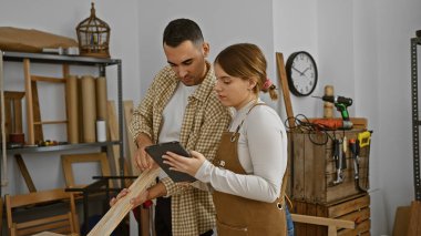 Bir adam ve bir kadın atölyede tablet kullanırken ahşap bir tahtayı değerlendiriyorlar..
