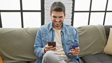 Akıllı telefon kullanırken gülümseyen ve modern oturma odasında kredi kartı tutan sıradan İspanyol bir adam..