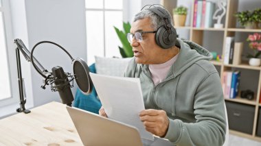 Orta yaşlı, kulaklıklı bir adam podcast stüdyosunda senaryo okuyor..