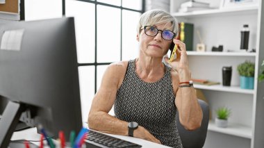 Ofiste telefon kullanan olgun bir kadın, profesyonellik ve güven gösterisi yapıyor..