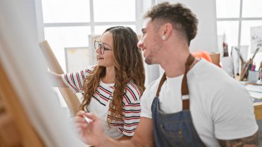 Erkek ve kadın sanatçılar, parlak bir stüdyoda işbirliği içinde resim yapıyorlar..