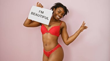 Confident young woman in red lingerie holding a 'i'm beautiful' sign against a pink background clipart