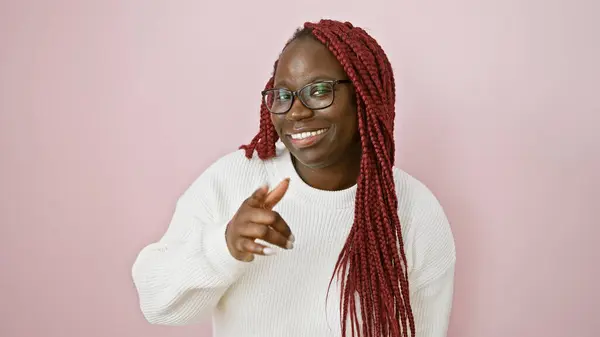 stock image Smiling african woman with braids pointing in a white sweater against a pink background