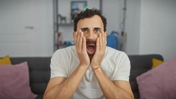 Stock image A surprised middle-aged man with a beard in a white shirt expressing shock in a modern living room.