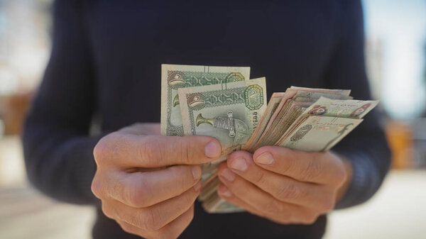 Взрослый человек, считающий единым арабом эмираты дирхамов на открытом воздухе в солнечной городской обстановке.