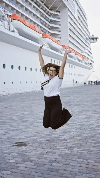 stock image A joyful woman jumps in excitement before boarding a cruise ship for a luxury voyage.