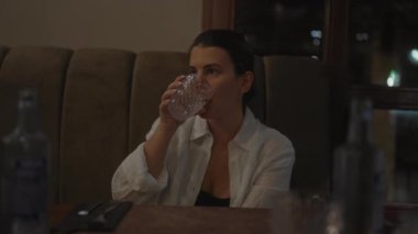 Loş ışıklı modern bir restoranda su içen düşünceli bir Latin kadın..