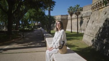 Güzel, genç, İspanyol bir kadın. Bari, İtalya 'da antik bir kalenin önünde oturuyor. Güneşli günün tadını çıkarıyor..