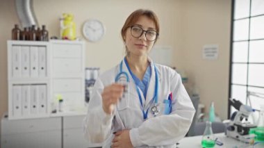 Klinikte steteskoplu, laboratuar önlüklü, kendinden emin genç bir kadın doktor.