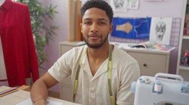 Gülümseyen Afrikalı adam terzide mezura, dikiş makinesi ve moda tasarım çizimleri ile