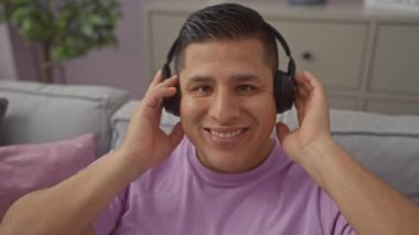 Gülümseyen bir İspanyol genç adam evdeki rahat oturma odasında kulaklıklarını çıkarıyor..