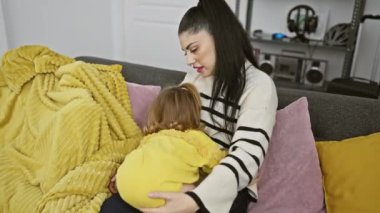 Sevgi dolu bir anne, küçük kızını sıcak bir kanepede kucaklar ve aile sevgisini gösterir..