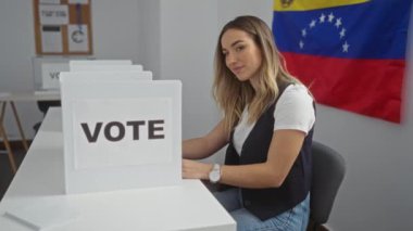 Venezuela 'da bir seçim kolejinde genç ve çekici bir sarışın kadın oy verme kabininin ve Venezuela bayrağının önünde baş parmak hareketi yaparken gülümsüyor..