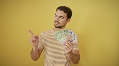 Neşeli, genç, İspanyol bir adam, kendine güvenen, gülümseyen ve neşeyle bir tarafı işaret eden. Güneşli sarı bir arka planda izole edilmiş.