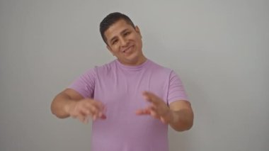 Genç İspanyol adam izole edilmiş beyaz arka planda duruyor, gülümsüyor ve elleriyle bir kalp yapıyor - aşkın ve romantik konseptin bir sembolü.