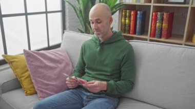 Kel ve sakallı adam içeride gri koltukta otururken para sayıyor..