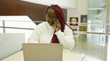 Modern ofis ortamında örgülü siyahi kadın telefonla konuşuyor.