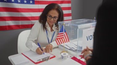 Amerikalı bir kadın oy verme merkezinde gönüllü olarak bayrak ve oy pusulalarını içeride taşıyor.