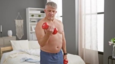 İyi dekore edilmiş bir yatak odasında dambılları kaldıran olgun, üstsüz bir adam orta yaşlarda sağlık ve zindeliğe işaret ediyor..