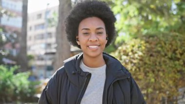 Afro-Amerikalı kadın, şehir parkında kulaklıkla neşeyle gülümsüyor..