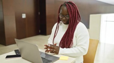 Örgülü siyah kadın modern ofiste dizüstü bilgisayar kullanıyor.