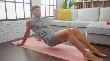 Genç zinde bir adam yoga yapıyor. Pembe bir paspas üzerinde ters duruş yapıyor. Şık bir oturma odasında, sağlığını ve sağlıklı bir yaşam tarzını gösteriyor..