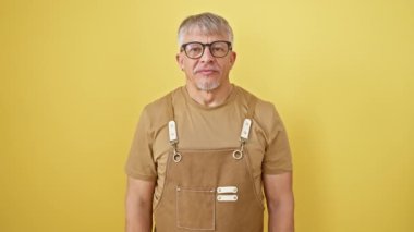 Küstah, orta yaşlı, gri saçlı, aşk dolu bir öpücük yollayan bir adam. Gözlük ve önlük takıyor, sarı arka planda duruyor, kameraya hem güzel hem de seksi görünüyor..