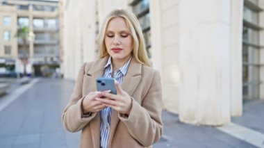 Şehir merkezinde açık havada dikilirken akıllı telefon kullanan çekici genç bir kadın..