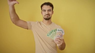 Sinirli, İspanyol asıllı genç bir adam, onaylanmamış eldivenli, sert sarı bir duvara karşı sert bir şekilde sallanıyor. Başparmakları aşağı işareti, finansal başarısızlıkların ve reddedilmenin açık bir sembolü..