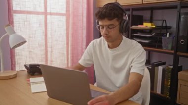 Ofisteki genç İspanyol bir adam, kulaklık takıp, dizüstü bilgisayar kullanarak profesyonel bir iş ortamı yaratıyor..