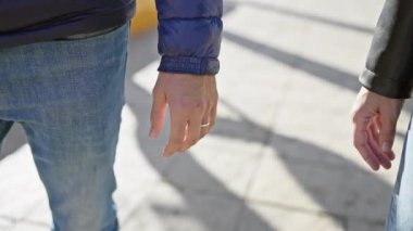 Güneşli bir şehir kaldırımında sevgi dolu bir jestle el ele tutuşan bir adam ve kadın..