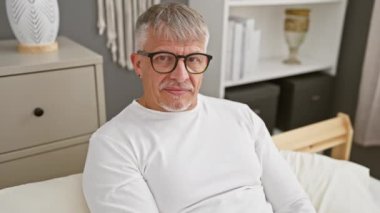 Orta yaşlı, gri saçlı, komik, seksi bir ifadeyle gülümseyen, pijamasında pençe hareketi yapan, rahat evinin yatak odasına agresif bir dönüş yapan bir adam.