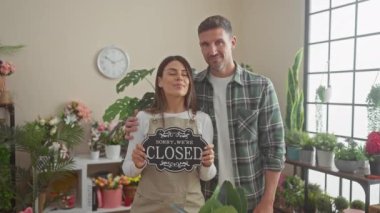 Bir erkek ve bir kadın, yemyeşil bir çiçekçinin ortakları, açık ve kapalı tabelalar arasında geçiş yapıyorlar, günlük iş hayatını resmediyorlar..