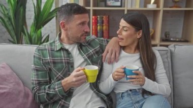 Sevgi dolu İspanyol bir çift, rahat bir oturma odasındaki rahat bir kanepede kahve fincanlarıyla rahatlıyor..