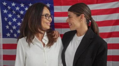 İki profesyonel kadın kapalı bir ortamda Amerikan bayrağına gülümsüyor, liderlik ve takım çalışması tasvir ediyorlar..