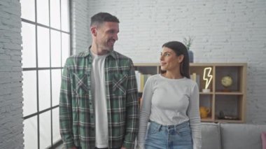 Oturma odasında gülümseyen İspanyol bir çift. Bir adam, parlak bir pencerenin arkasında bir kadına sarılıyor..