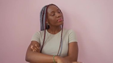 Neşeli Afro-Amerikalı kadın kendine güvenerek ayakta duruyor, güzel bir gülümseme sergiliyor ve görünmez bir ürünü soyutlanmış pembe bir arka plana işaret ediyor..