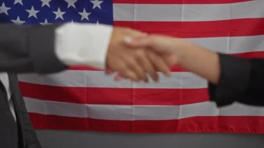 İki profesyonel, Amerikan bayrağı önünde el sıkışıyor. Birleşmiş Milletler ofisinde işbirliği ve liderliği simgeliyor..