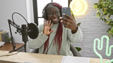 Örgülü Afrikalı Amerikalı bir kadın radyo stüdyosunda mikrofon ve neon ışıklarla video görüşmesi yapıyor..