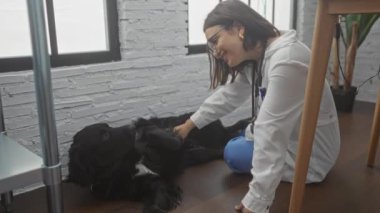 Veteriner kliniğindeki Latin kökenli genç bir kadın siyah bir labradoru evdeki bir yerde nazikçe önemsiyor..