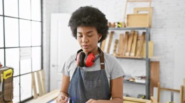 Bir marangoz atölyesinde güvenlik gözlüğü ve kulaklık takan Afrikalı Amerikalı kadın.