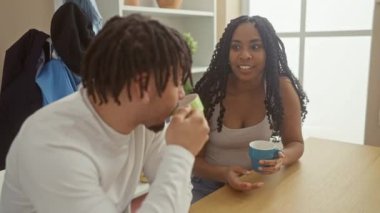 Bir erkek ve bir kadın, rahat bir oturma odasında neşeyle sohbet eder, kahkahalar ve içkileri paylaşır, rahatlamış bir aile ortaklığını somutlaştırır..