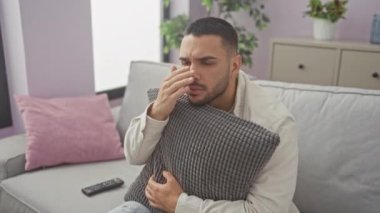 Genç bir İspanyol adam oturma odasındaki kanepede oturuyor, gözü kaşınırken elinde bir yastık tutuyor..