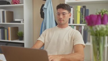 Yakışıklı İspanyol adam gözlüğünü çıkarıp modern bir evin içinde kameraya gülümsüyor..