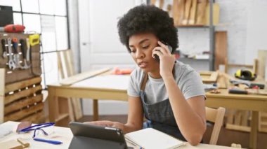İş için tablet kullanan Afrikalı Amerikalı kadın atölyede telefonla konuşuyor.