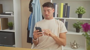 Modern bir ev ofisinde bitkiler ve kitaplarla akıllı bir telefonla konuşan şık bir genç..