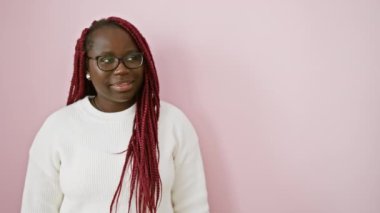 Örgü örgülü neşeli bir Afrikalı Amerikalı kadın soyutlanmış pembe bir arka plana karşı yan bakıyor.
